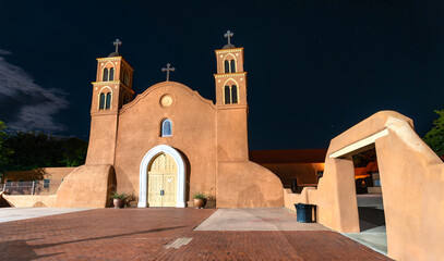 Fototapeta premium Old San Miguel Mission church in Socorro, New Mexico. Historic adobe architecture features twin towers and a white arch entrance under a starry night sky