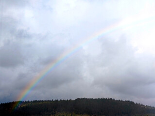 Rainbow against a gray blue sky over a mountain forest