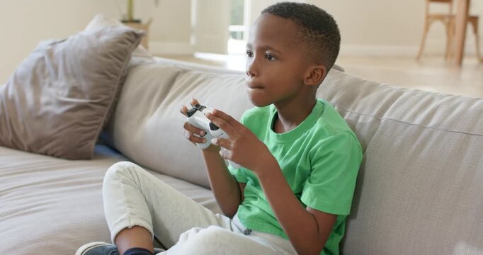 African American boy reacting to game, sitting at home, holding white controller, trying to win