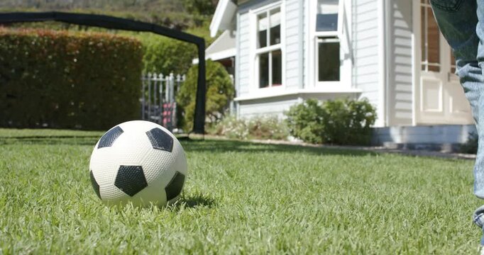 Child is positioning foot beside soccer ball on grassy lawn, tapping and aiming shot toward goal