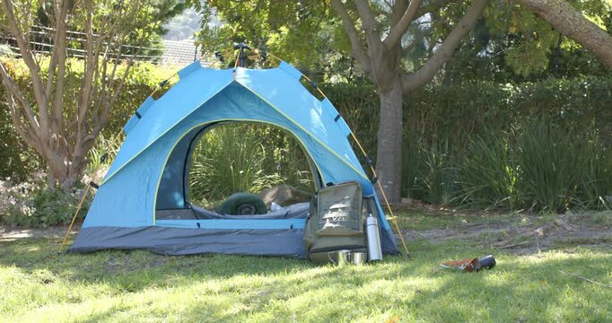 African American father and child resting in blue tent after pitching, backpack, thermos beside