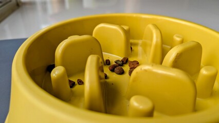 A yellow puzzle feeder for pets with some kibbles or cat food inside © Jullian