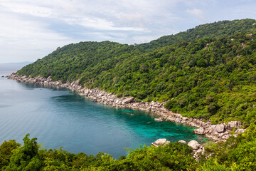Lighthouse Bay, Koh Tao, Thailand. Tropical rocky coastline with clear blue water. Lush green forest and scenic seascape. Ocean meets the shore under a cloudy sky.