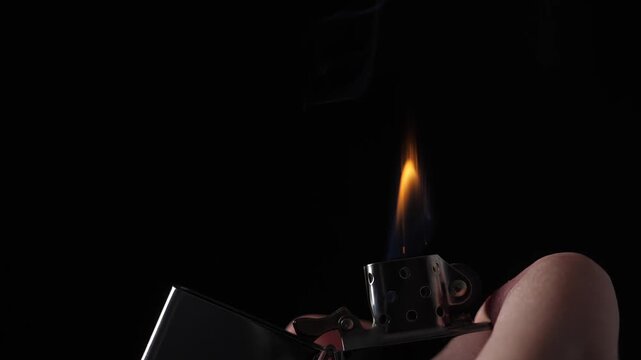Igniting gasoline lighter with flying sparks on black background, closeup. Burning flame in slow motion