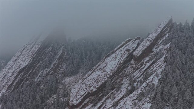 Winter lightly snowing fog Flat Irons rock formations slabs Chautauqua Park trail Boulder Colorado aerial drone sunset dusk evening snowy trees snow falling foggy grey skies low cloud layer forward
