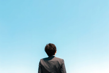 広大な空を仰ぐ男性会社員。無限の可能性、キャリアの成功、リフレッシュを象徴するイメージ