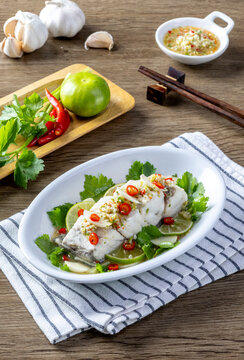 Steamed sea bass with lemon sauce served on a wooden table.