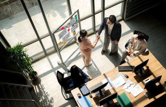 Top view of business colleagues shaking hands during a meeting near a presentation board