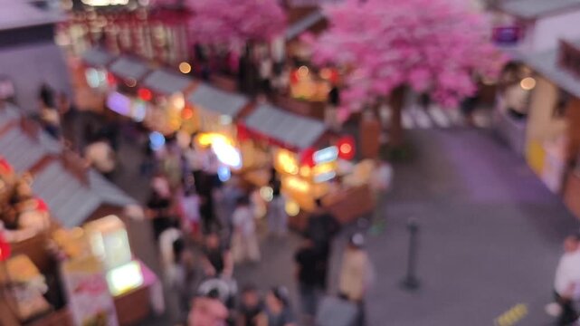 4K video footage. High-angle blurred of vibrant Japanese-style night market or food festival featuring stalls with red lanterns and cherry blossoms