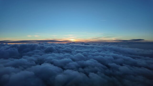 Immersive pilot POV of a twilight scene while flying over an endless blanket of stratus clouds and the sun sinking beyong a golden horizon.