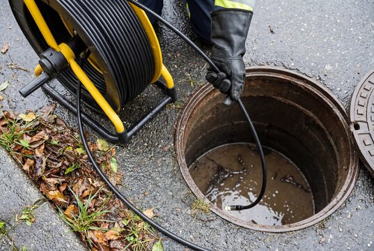 Worker with gloved hand inserting a flexible inspection camera probe into an open manhole