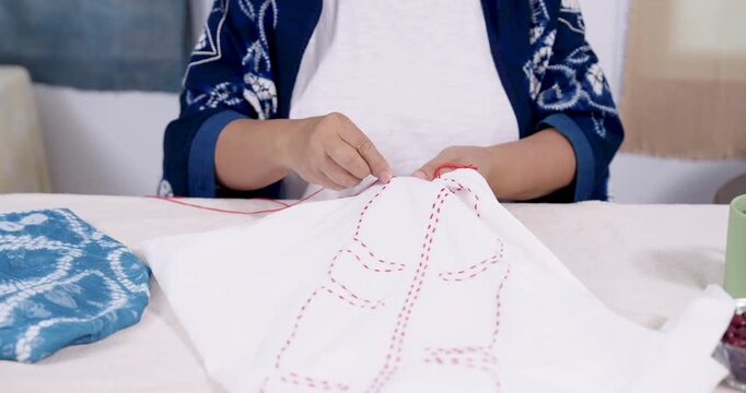 Close up hands pull needle through cotton cloth, forming resist stitching lines for Japanese shibori tie dye, senior Asian craftswoman making sustainable textile for boutique order, natural dye.
