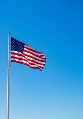 National flag of the United States of America waving in the wind against a clear blue sky. Symbol of freedom, democracy and independence. Background with copy space for text.