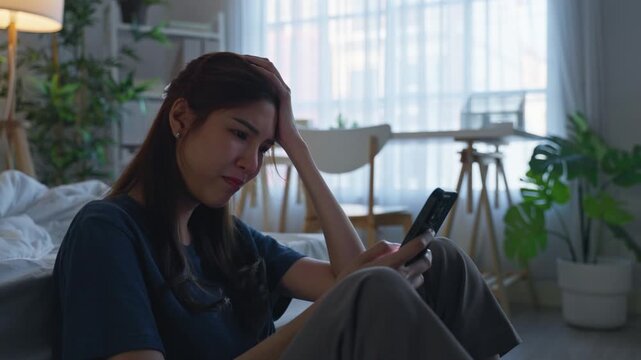 Asian young depressed woman looking at mobile phone in bedroom at home.