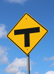 Yellow T‑intersection warning sign against a blue sky with scattered clouds