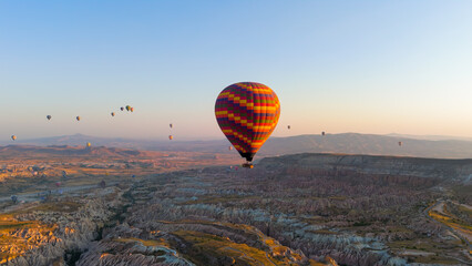 Goreme, Nevsehir, Turkey. Single large colorful checkered hot air balloon with yellow red orange purple colors isolated against bright morning sky over Cappadocia. Aerial View © Video Render