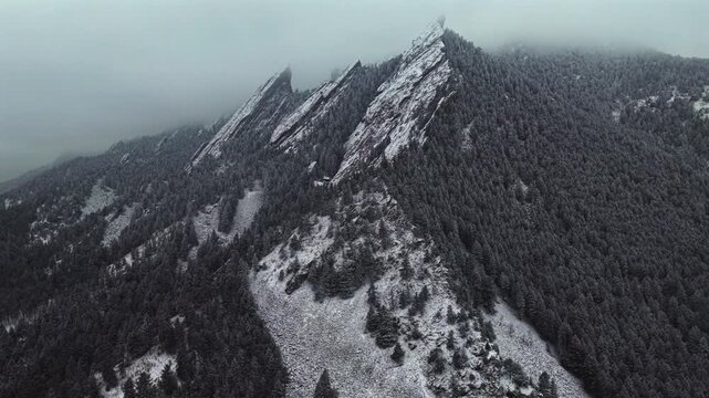 Winter snowing fog Flat Irons rock formations slabs Chautauqua Park trail aerial drone Boulder Colorado sunset dusk evening snowy trees snow falling foggy grey skies low cloud layer forward pan motion