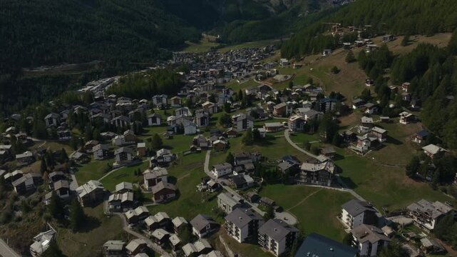 Aerial drone footage of the town of Saas-Fee with views over Allalin, Saas-Allmagell and Saas-Grund on a clear bluebird autumn day. Green valley floor contrasts with snow-covered alpine peaks.