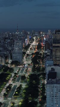 Vertical aerial pan left showing Avenida 9 de Julio with traffic flow and the iconic Evita Building in Buenos Aires Argentina at night.