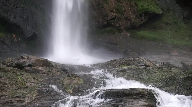 Natural waterfall at Akchour flowing over layered rocks with strong stream movement surrounded by green forest creating peaceful scenic landscape in northern Morocco