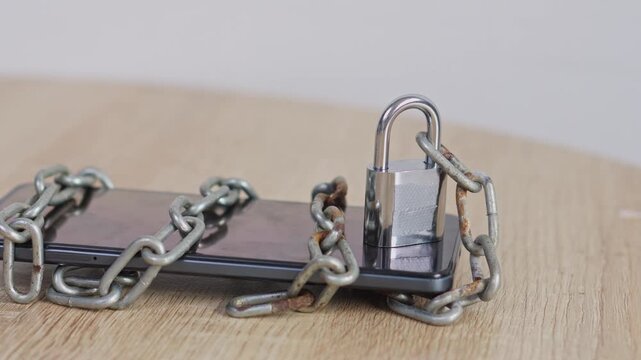 Smartphone secured with metal padlock and rusty chains on wooden surface