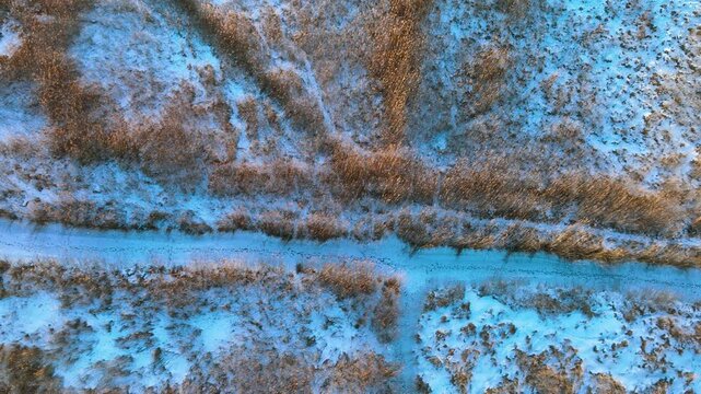 Cinematic drone shot showing a topdown perspective of frozen reeds and snowcovered ground in Rewa, Poland. Perfect for winter travel and nature documentaries.