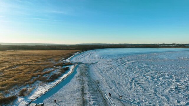A stunning drone shot of the frozen Baltic Sea coast in Rewa, Poland, featuring snowcovered shores and golden reeds under a clear blue sky.