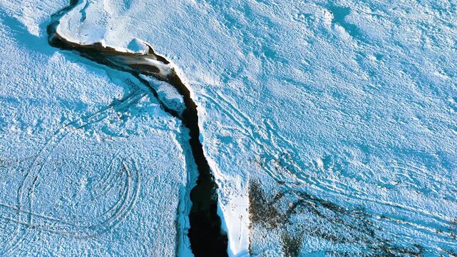 A cinematic birds eye view of a dark winding river cutting through a thick white snow covered landscape in Rewa, Poland. Perfect for winter travel and nature documentaries.