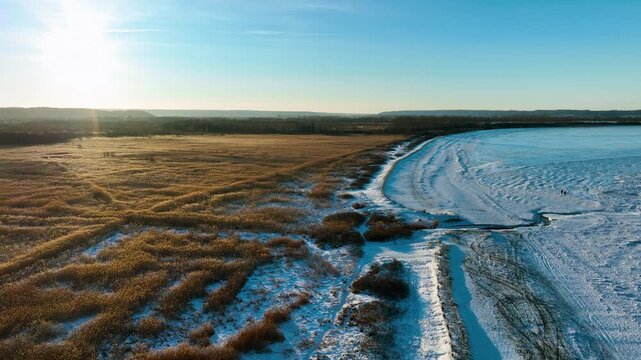 Stunning aerial footage of a winter landscape in Rewa, Poland, featuring frozen sea ice meeting golden reed fields under a bright morning sun. Ideal for travel and nature documentaries.