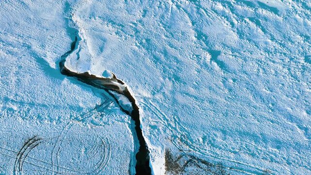 High angle drone shot of a dark winding river cutting through a snow covered landscape in Rewa, Poland. Perfect for winter travel and environmental documentaries.