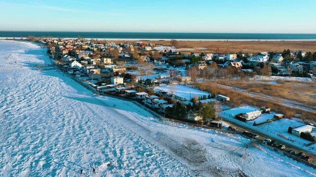 Stunning aerial drone footage of a snowy coastal village in Rewa, Poland, featuring a frozen sea and winter landscape. Ideal for travel documentaries and seasonal marketing.
