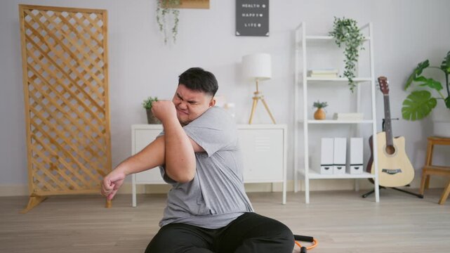 Exhausted Asian plus-size man workout and try to stretching arm on yoga mat.