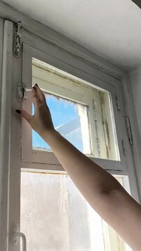 A woman's hand opens the window of an old wooden window to ventilate the room, the house. Fresh air in the house