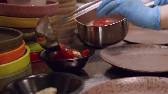 Preparing soup. Portioned dish. Chef hand pouring hot red liquid meal in bowls standing row. Serving borsch on restaurant kitchen table.