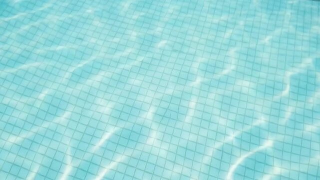 Closeup view of clear blue pool water with tile pattern and sunlight reflections