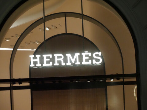Brightly lit Hermes branding sign on an arched window of a luxury store in Warsaw