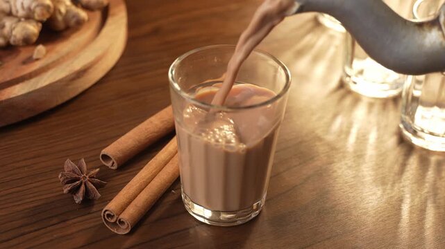 Indian chai served in glass cups, brewed in a metal kettle with aromatic masalas. Getting poured on glass.