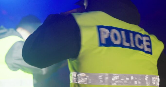 police officers from behind wearing high-visibility vests during a night operation, symbolizing law enforcement teamwork, public safety, emergency response, and serious police action in low-light cond