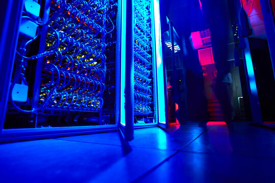  Low angle view of glowing blue server aisles in futuristic high density data center corridor highlighting powerful computing clusters and critical digital infrastructure