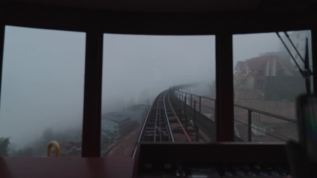 Curved Muong Hoa funicular railway disappearing into dense fog in the mountains of Sapa, Vietnam. Atmospheric public transport scene with low visibility and misty weather.