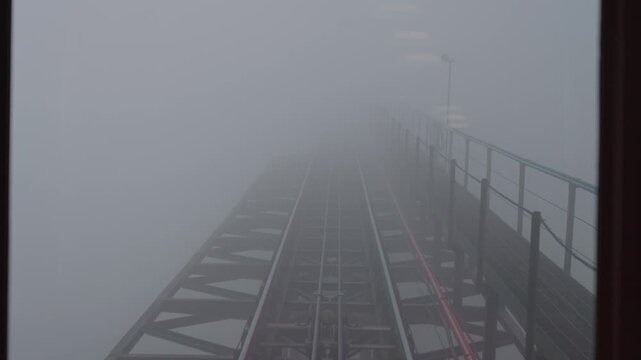 Curved Muong Hoa funicular railway disappearing into dense fog in the mountains of Sapa, Vietnam. Atmospheric public transport scene with low visibility and misty weather.