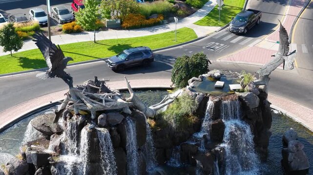 A drone view of a roundabout with a sculpted fountain at its center, surrounded by manicured landscaping and roads in Idaho Falls