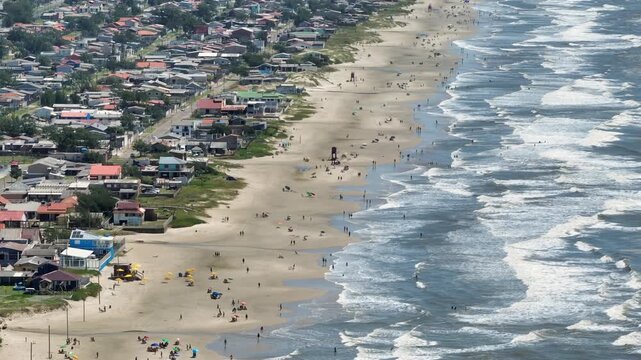 Telephoto 7x drone hover tilt up reveal from busy beach to wide coastline and horizon in Balneario Pinhal, Brazil.