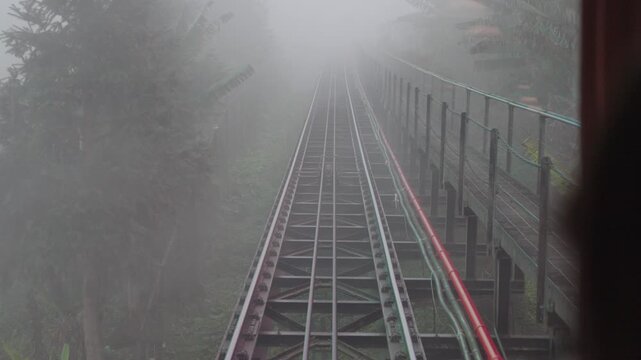 Curved Muong Hoa funicular railway disappearing into dense fog in the mountains of Sapa, Vietnam. Atmospheric public transport scene with low visibility and misty weather.