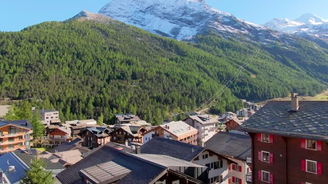 Aerial rise above captivating close-up of Saas-Fee, Switzerland &ndash; colorful chalets and cozy homes nestled against lush green forests and towering snow-capped peaks