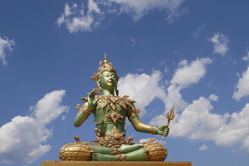 Magnificent green Buddha adorned with golden ornaments against a bright blue sky with white clouds. Serene, photogenic composition symbolizing spirituality, peace, harmony, and sacred beauty.