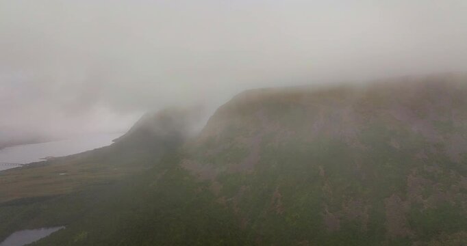 Sortland hills and rugged terrain fade into dense fog with layered slopes and muted northern tones, aerial reveal through clouds