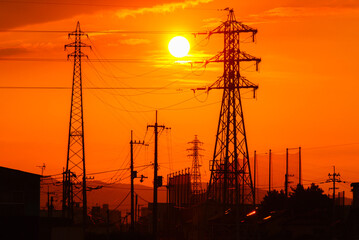 夕焼けの太陽と送電線のシルエット　電力インフラと都市風景