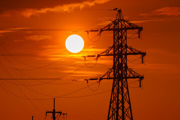 夕焼けの太陽と送電線のシルエット　電力インフラと都市風景