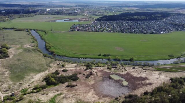 High angle vista of a meandering river carving through verdant fields, with a sprawling dacha settlement nestled across the bank. Protva river, Kaluga region, Russia